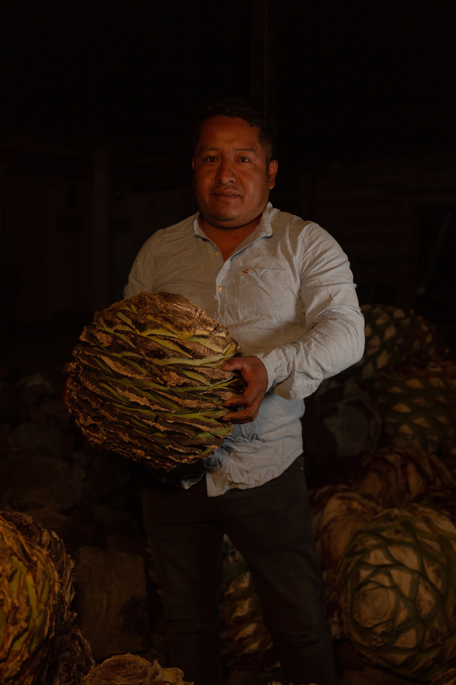 Image of Jose Manuel Mendez in distillery holding Fuego Y Humo roasted piña.